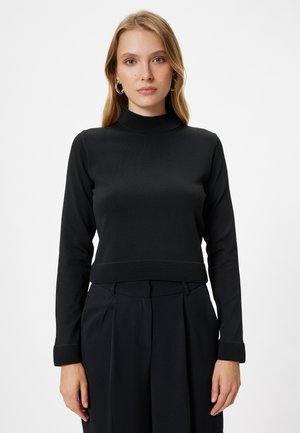 Haut noir en tricot à manches longues avec un col montant et un ourlet côtelé. Tissu texturé avec un design ajusté, associé à un pantalon taille haute.