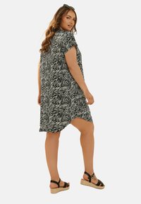 Svartvitt zebramönstrad klänning med korta ärmar, en avslappnad passform och rundad nederkant, kombinerad med svarta sandaletter med remmar och espadrillos.