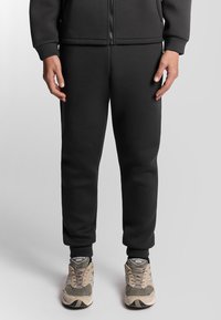 Zwarte joggingbroek met een elastische tailleband en boorden, gemaakt van een glad, zacht materiaal. G gedragen met grijze en beige sneakers.