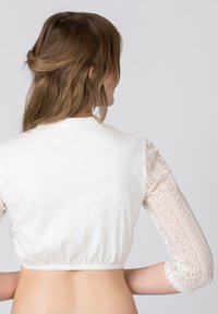 White cropped top with a smooth cotton body and sheer lace long sleeves, featuring a gathered hem and detailed lace patterns.
