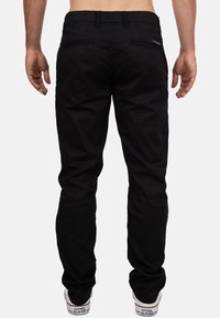 Pantaloni in tessuto nero con una vestibilità dritta, caratterizzati da due tasche posteriori, cuciture sottili e una vita standard, indossati con sneakers bianche.