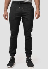Pantalones de chándal negros con cintura elástica, cierre con cordón, bolsillos laterales y puños acanalados. Fabricados en una tela suave.