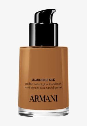 Luminous Silk foundation in een doorzichtig glazen flesje met een bruine tint. Heeft een zwart pompdeksel en zwarte bedrukte etiketdetails.