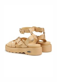 Sandali platform beige con cinturini incrociati, fibbia regolabile alla caviglia e suola in gomma texture. Punta arrotondata e interno morbido.