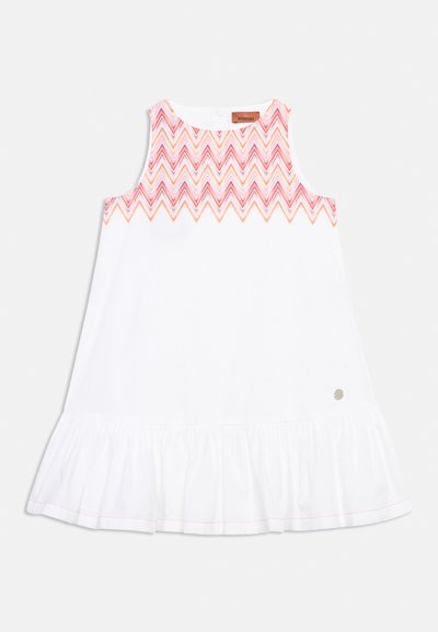 Robe blanche sans manches avec un ourlet à volants et un motif chevron rose, orange et violet sur la poitrine et les épaules.