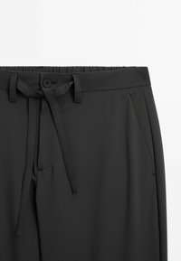 Pantalons gris foncé en tissu léger. Comprend une taille élastique, un bouton à l'avant et un lien à tirer. Texture lisse avec un minimum de détails.