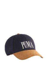 Gorra de béisbol azul marino con visera de ante marrón, que presenta letras blancas de "PUMA" en la parte frontal. Textura de tela suave, forma estructurada.
