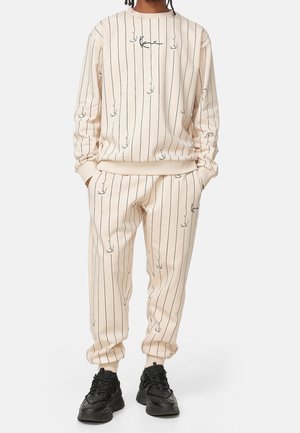 Set di felpa e pantaloni beige con strisce nere verticali e una stampa sottile simile a piante. Il materiale sembra morbido, con polsini e vita elasticizzati.