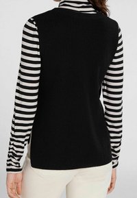 Zwarte geribbelde tanktop met hoge hals, gedragen over een zwart-wit gestreepte lange mouw shirt. Glad textuur, aansluitend ontwerp.