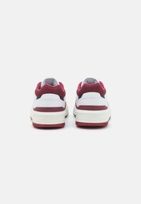 Fehér és burgundi színű sneaker, textil felső résszel, párnázott sarkal és gumitalppal. A saroknál logó található, fekete kiegészítőkkel.