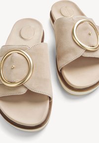 Sandalias beige de ante deslizantes con correas anchas cruzadas y grandes hebillas circulares doradas sobre suelas blancas de plataforma.