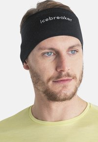 Mężczyzna z jasną bródką, noszący czarną opaskę na głowie z napisem "icebreaker" i jasną żółtą koszulę, lekko patrzący w prawo.