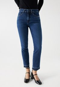 Vaqueros de denim azul oscuro con ajuste slim, cintura alta y longitud cropped, que presentan costuras sutiles y un ligero detalle de dobladillo deshilachado.