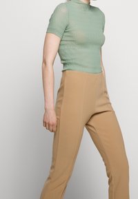 Light green, fitted short-sleeve top with a textured pattern, paired with high-waisted beige pants featuring side seams and a smooth finish.