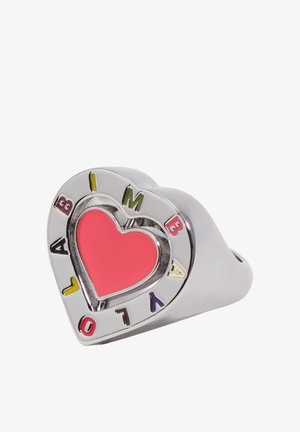 Anillo plateado en forma de corazón con un centro de corazón rojo y letras coloridas que forman la palabra "AMBIVALO" alrededor del borde sobre un fondo blanco.
