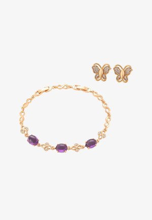 Arany karkötő lila drágakövekkel és strassz díszítésekkel, párosítva arany pillangó alakú fülbevalókkal, amelyeket strasszok díszítenek.