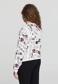 Felpa bianca con grafiche colorate, che presentano testo e illustrazioni. Polsini e orlo a coste. Indossata con leggings neri.