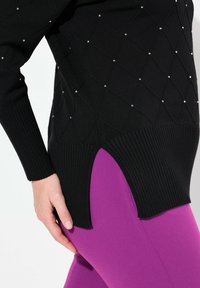 Svart tröja med diamantmönster och små nitar, med ribbad fåll. Tillsammans med lila leggings som har sidssprund.