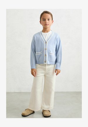Lyseblå cardigan med hvide kantdetaljer, med V-hals, knapper ned foran og to forlommer. Kombineret med cremefarvede bukser med vide ben.