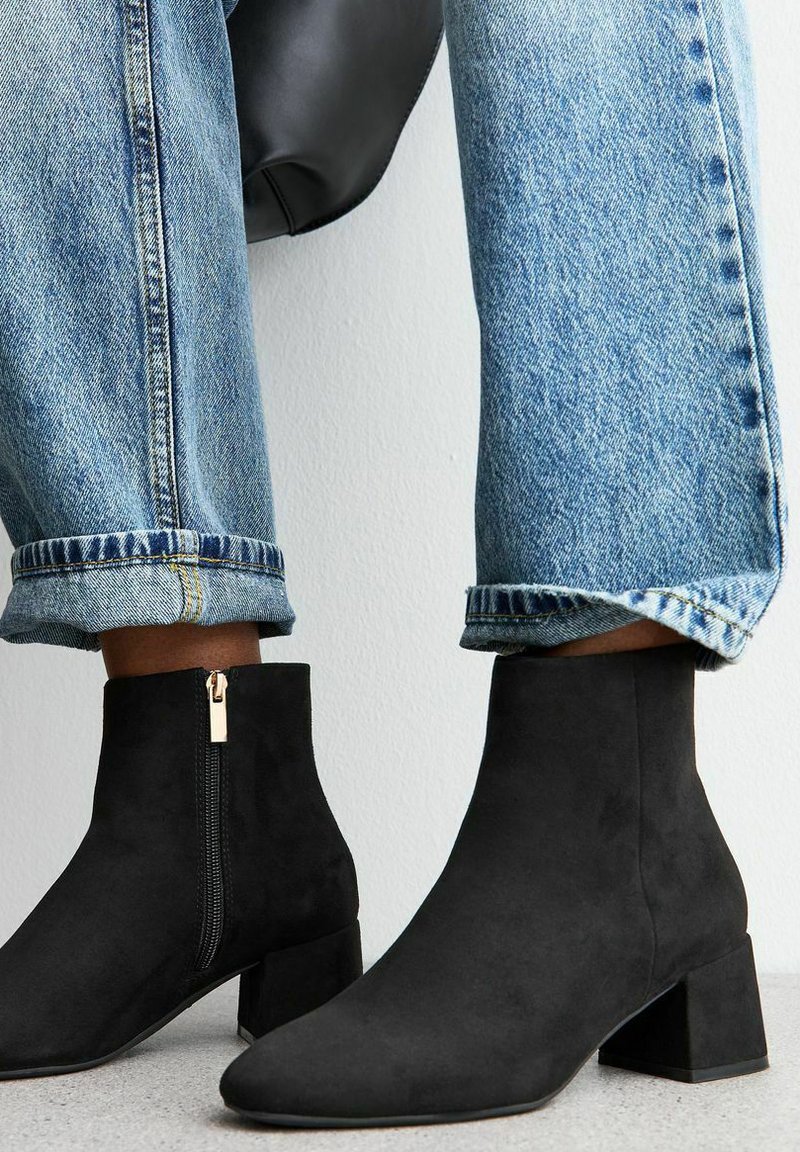Zwarte suède enkellaarsjes met een lage blokhak en een rits aan de zijkant, gecombineerd met opgerolde blauwe jeans, wat een casual uitstraling geeft.
