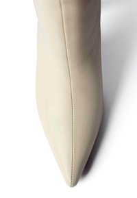 Beežid nahast kõrge kontsaga king, millel on terav nina ja sile tekstuur. Poolt joon, mis jookseb mööda külge, lisab disainile detaili.