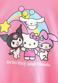 Vaaleanpunainen graafinen T-paita, jossa on Hello Kitty ja ystävät, piirros hahmoista, jotka pitävät ilmapalloista ja sateenkaaresta, rohkeat mustat ääriviivat ja leikkisä teksti.