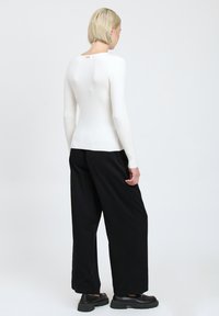 Pullover bianco a costine con una forma aderente e maniche lunghe, abbinato a pantaloni neri larghi e scarpe nere chunky. Accenti di design minimal.