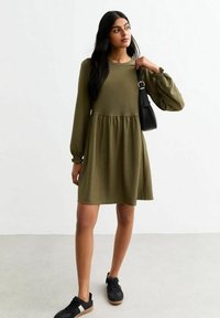 Olive green dress z długim rękawem, teksturowany materiał, dopasowany gorset i rozkloszowana spódnica. Połączona z czarnymi sneakersami i małą torebką.