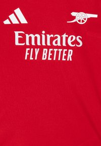 Rotes Sporttrikot mit weißen Logos: "Emirates" und "FLY BETTER", sowie einem Arsenal-Kanonen-Logo. Hergestellt aus leichtem, glattem Stoff.