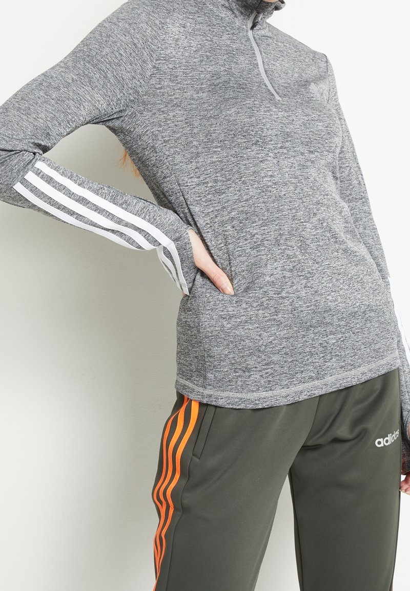 Szary długi rękaw top z kołnierzem na pół zamek, z białymi paskami na rękawach. Połączony z zielonymi spodniami z pomarańczowymi paskami.