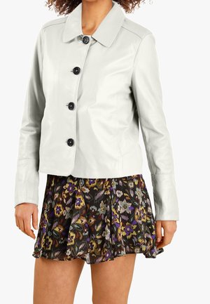 Hellgraue Lederjacke mit Kragen, Frontknöpfen und langen Ärmeln, kombiniert mit einem fließenden schwarzen Rock mit Blumenmuster.