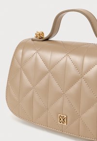 Bežs iešūts ādas soma ar strukturētu formu, viena roktura un zelta akcentiem. Izteikta dimanta raksts un izšūšanas detaļas.