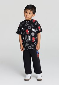 Czarna koszulka z kolorowymi grafikami Spider-Mana oraz symbolami z komiksów, w zestawie z czarnymi spodniami z czerwonym i niebieskim wzorem Spider-Mana.