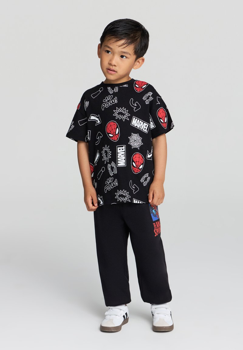 Czarna koszulka z kolorowymi grafikami Spider-Mana oraz symbolami z komiksów, w zestawie z czarnymi spodniami z czerwonym i niebieskim wzorem Spider-Mana.