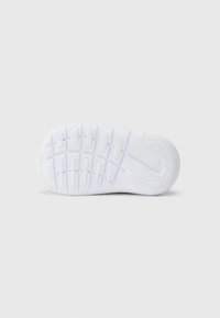 Valkoinen kuminen urheilukenkiä pohja, jossa on teksturoitu pito-kuvio ja keskeinen Nike-logo. Sisältää riveittäin kohotettuja harjanteita pitoa varten.
