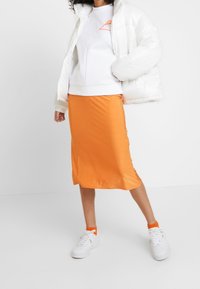 Giacca a vento bianca, gonna midi arancione e scarpe da ginnastica bianche con accenti arancioni. Texture lisce ed elementi di design moderni e casual.