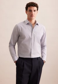 Hellblaues, knopfbares Hemd mit dezentem geometrischen Muster, langen Ärmeln und einer Brusttasche. Kombiniert mit dunklen Hosen.