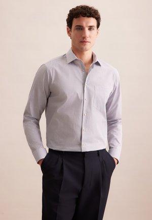 Lichtblauw overhemd met lange mouwen en een subtiel geometrisch patroon, voorzien van een borstzak. Gecombineerd met donkergekleurde broek.