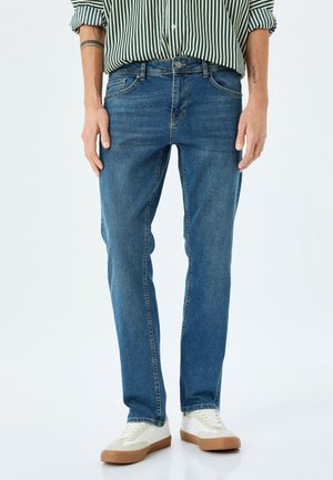 Bleu denim jeans met een recht model, voorzien van voorzakken, subtiele stikdetails en een versleten textuur, in combinatie met witte sneakers.