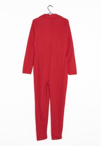 Czerwona kombinezon na wieszaku, z kołnierzykiem, długimi rękawami i dopasowanymi nogawkami. Gładki materiał z bezszwowym wzornictwem.
