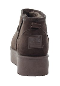 Brązowy zamszowy botek za kostkę z teksturowaną powierzchnią, wyściełanym kołnierzem i naszywką z logo; posiada grubą podeszwę i przeszycia.