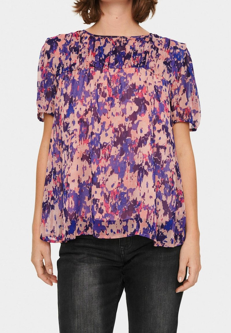 Genomskinlig blus med kort ärm i ett mönster av flera färger i rosa, lila och blått. Har rund halsringning och en lös, flödande passform.
