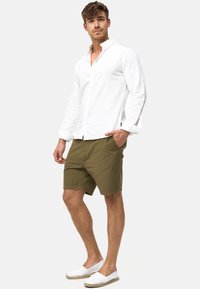 Hvid langærmet skjorte, grønstribede shorts og hvide espadrillos. Outfitet har en afslappet pasform og letvægtsstof.