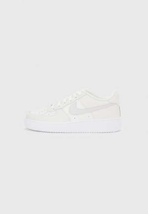 Baskets basses blanches avec embout perforé, logo swoosh blanc, et semelle blanche épaisse, vues de côté sur fond uni.
