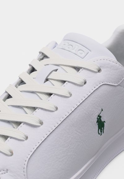 Λευκό δερμάτινο αθλητικό παπούτσι με λευκά κορδόνια, πράσινο λογότυπο Polo Ralph Lauren με άλογο και αναβάτη στο πλάι, και ανάγλυφο «Polo» στη γλώσσα του παπουτσιού.