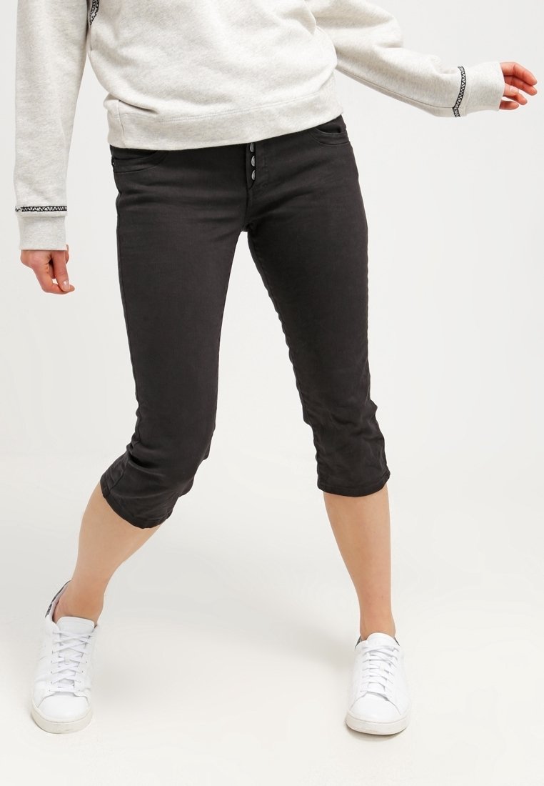 Personne portant un pantalon court noir et des baskets blanches, debout, jambes écartées et bras légèrement étendus.