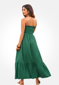 Abito lungo verde senza spalline con un corpetto arricciato, pieghe verticali e orlo arricciato. Il tessuto appare leggero e ha una texture liscia.