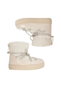 Světlé béžové zimní kotníkové boty s robustními podrážkami, prošívanými svršky a obepínajícími šňůrkami, zobrazené vedle sebe na bílém pozadí.