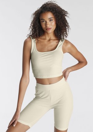 Light beige ribbed crop top with square neckline, paired with matching high-waisted bike shorts, made from stretchy fabric.