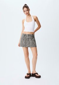 Un top halter blanc et une jupe en denim léopard grise. La jupe a cinq poches et une fermeture à bouton. Des sandales noires à plateforme complètent la tenue.